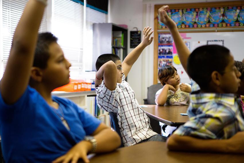 Three students raising their hands in  a classroom